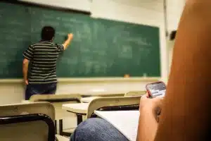 Schultische mit Rucksäcken, Prüfungsunterlagen und Uhr in einem Klassenraum