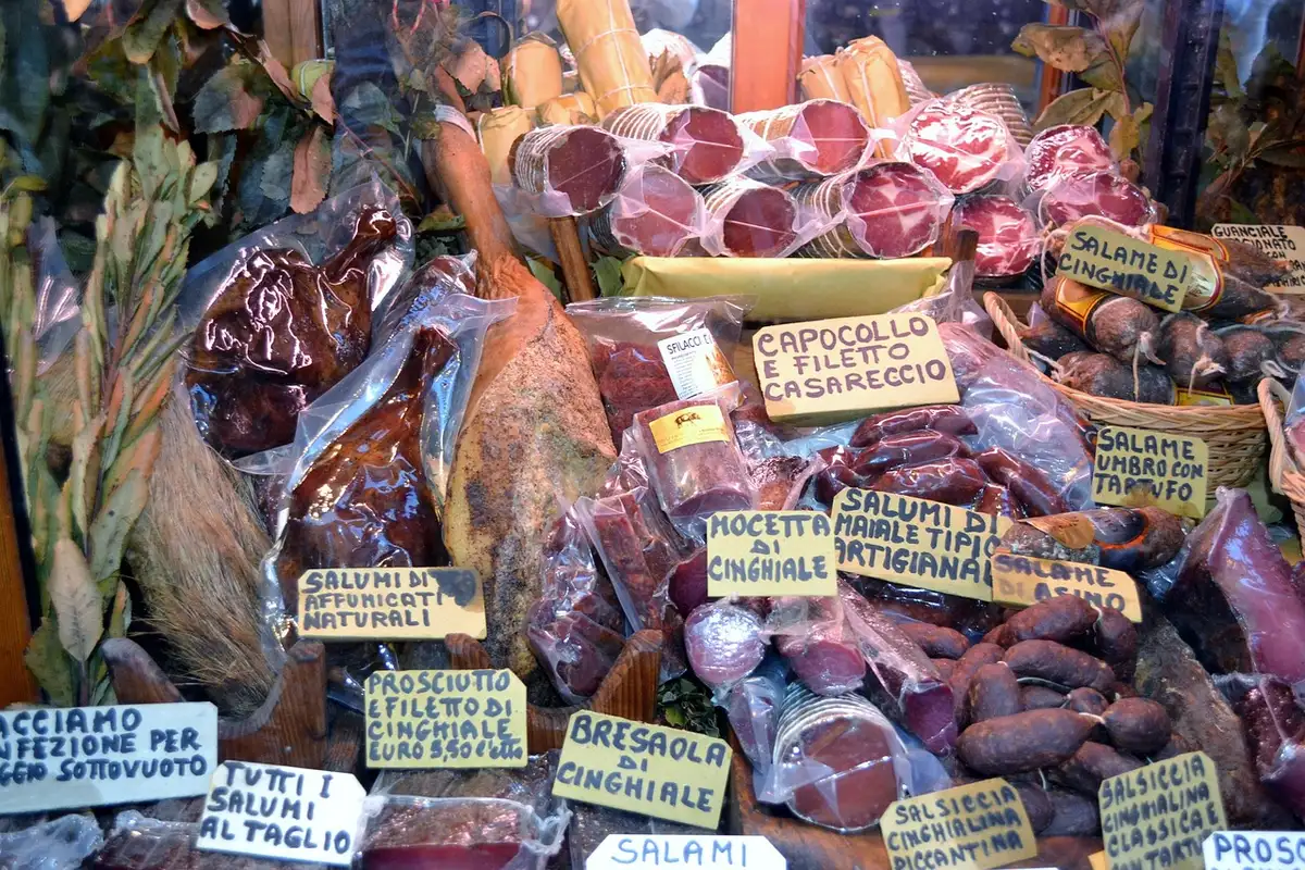 Lehrling schneidet Fleisch unter Aufsicht in einer Metzgerei